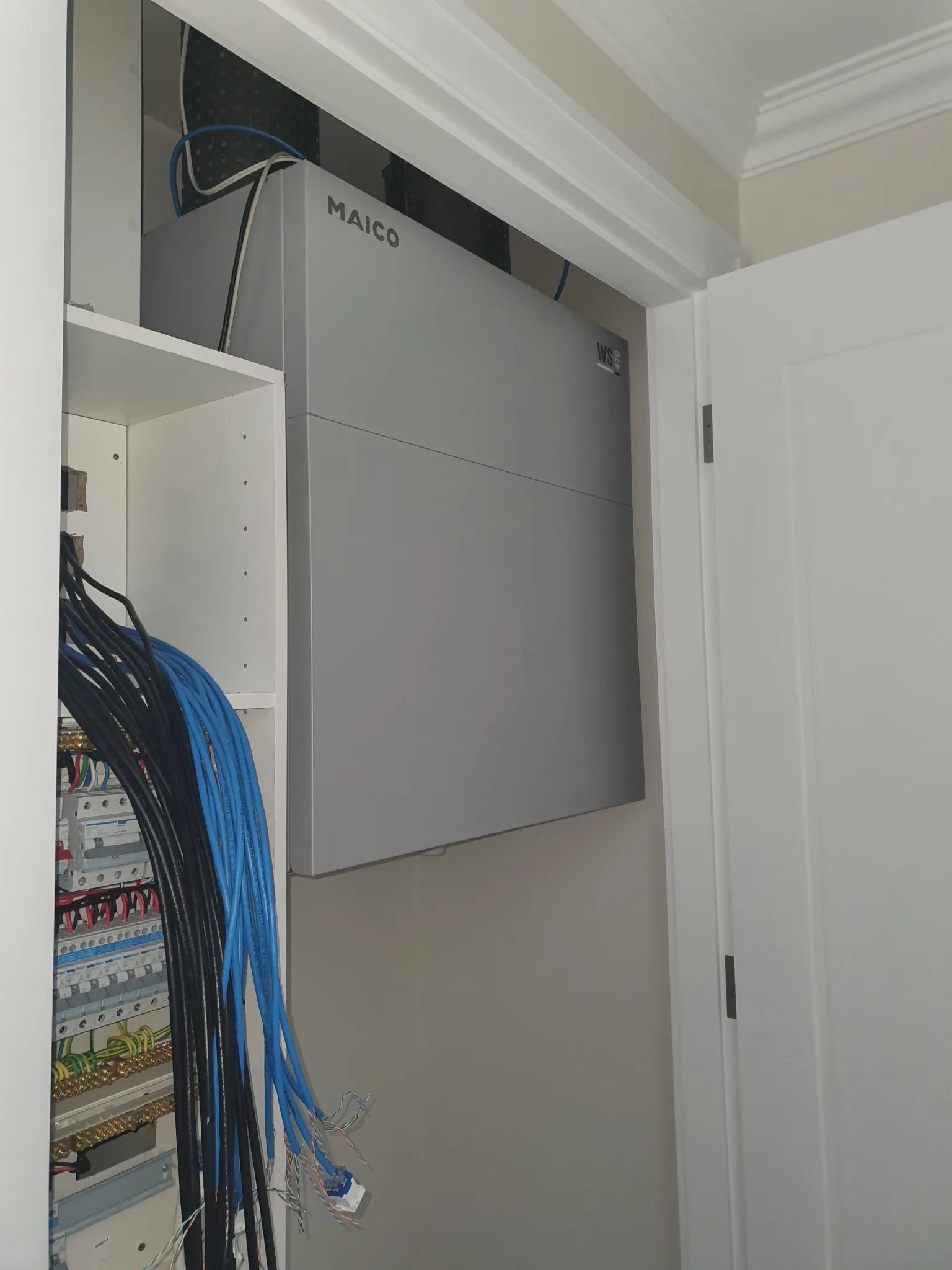 Wall-mounted heat recovery ventilation unit installed in a cupboard beside the electrical board